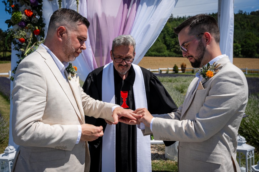 Výměna prstenů při obřadu před vyzdobenou svatební bránou